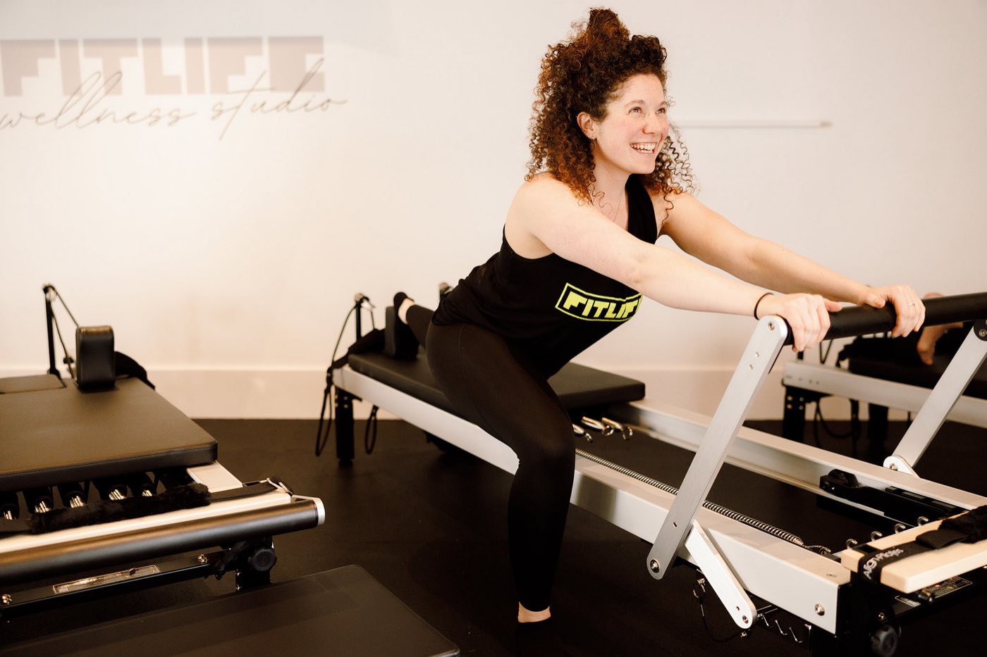 Ashton on a reformer bed at FitLife wellness studio, drawing the carriage back on the footbar