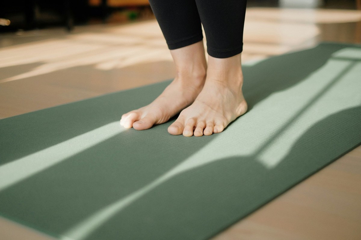 Bare feet grounded on a sage-green yoga mat in soft light